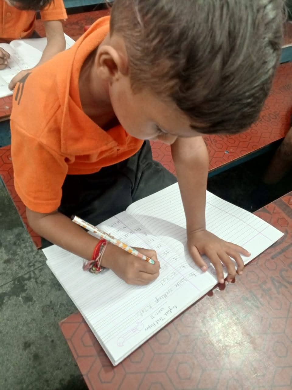 Close-up of a child in orange uniform writing in their workbook